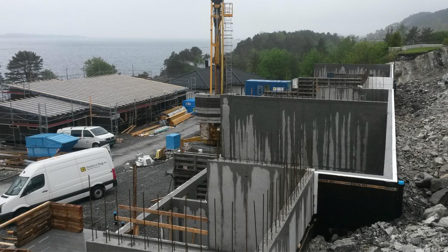 Concrete walls going up on a building site by the fjord, with a crane and vans