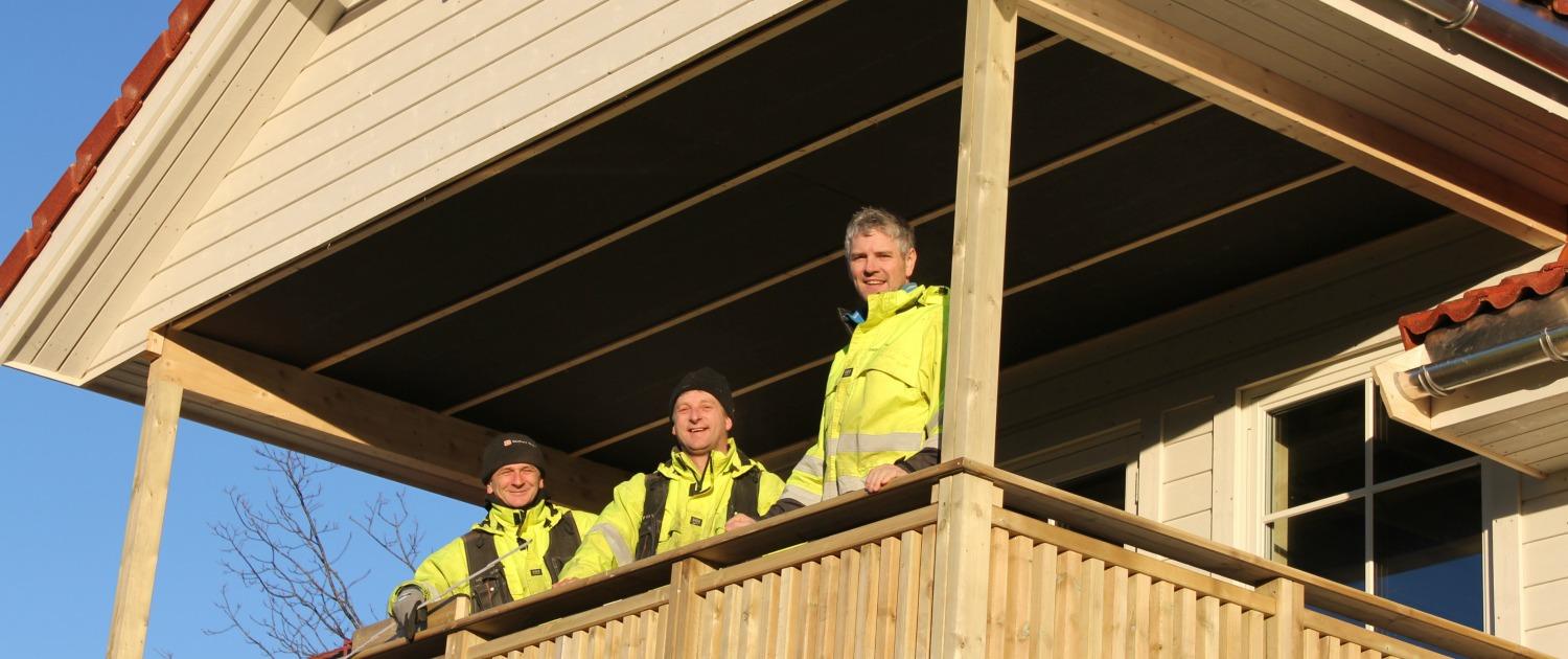 Three of the crew in hi-vis jackets on the veranda of a house they built