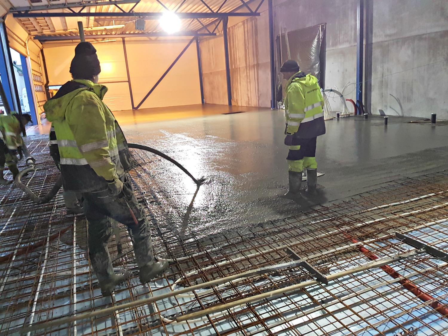 Two workers in hi-vis pouring a concrete floor over reinforcement mesh